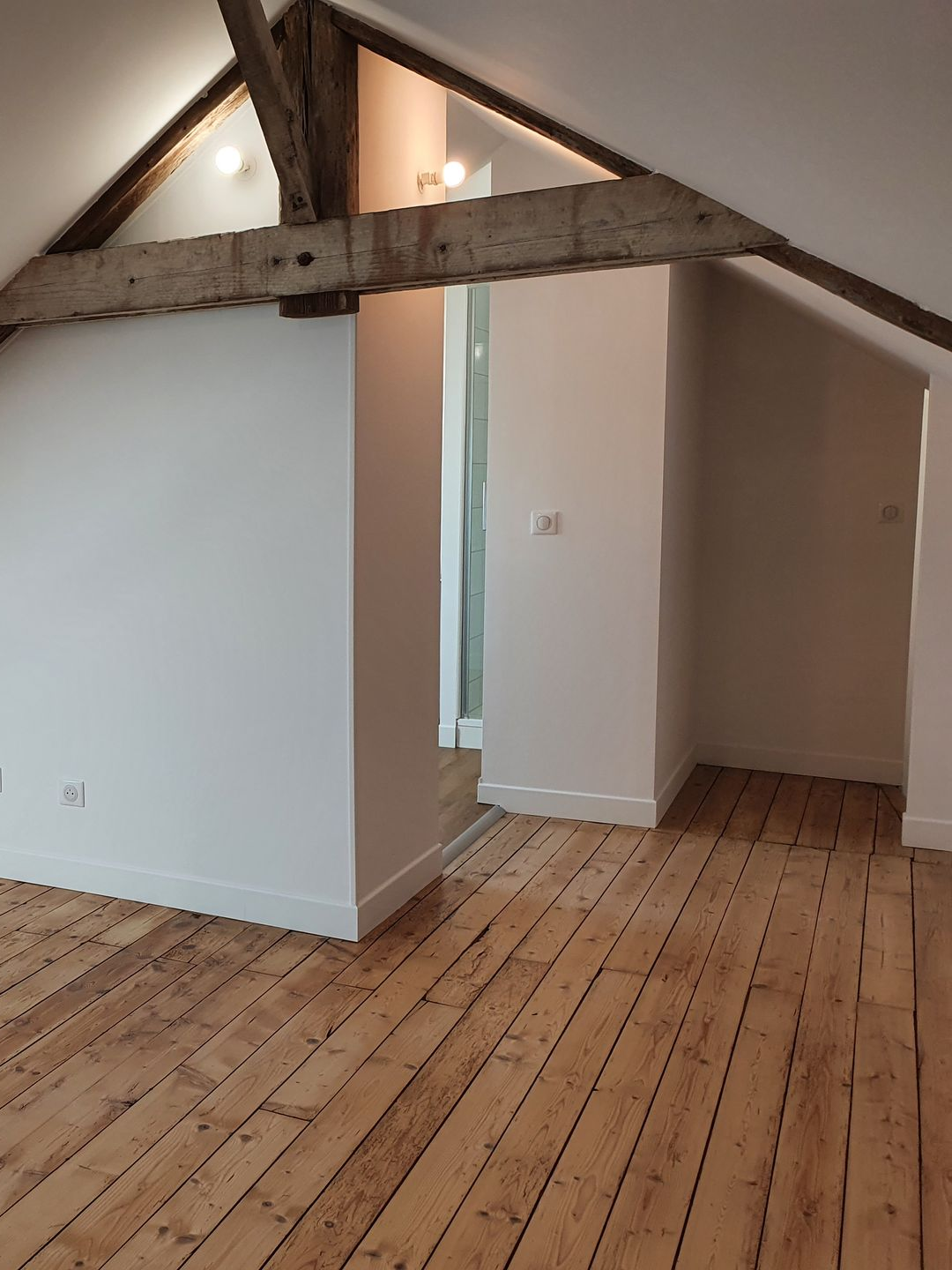 Pièce avec parquet, murs blancs, poutre apparente et porte.