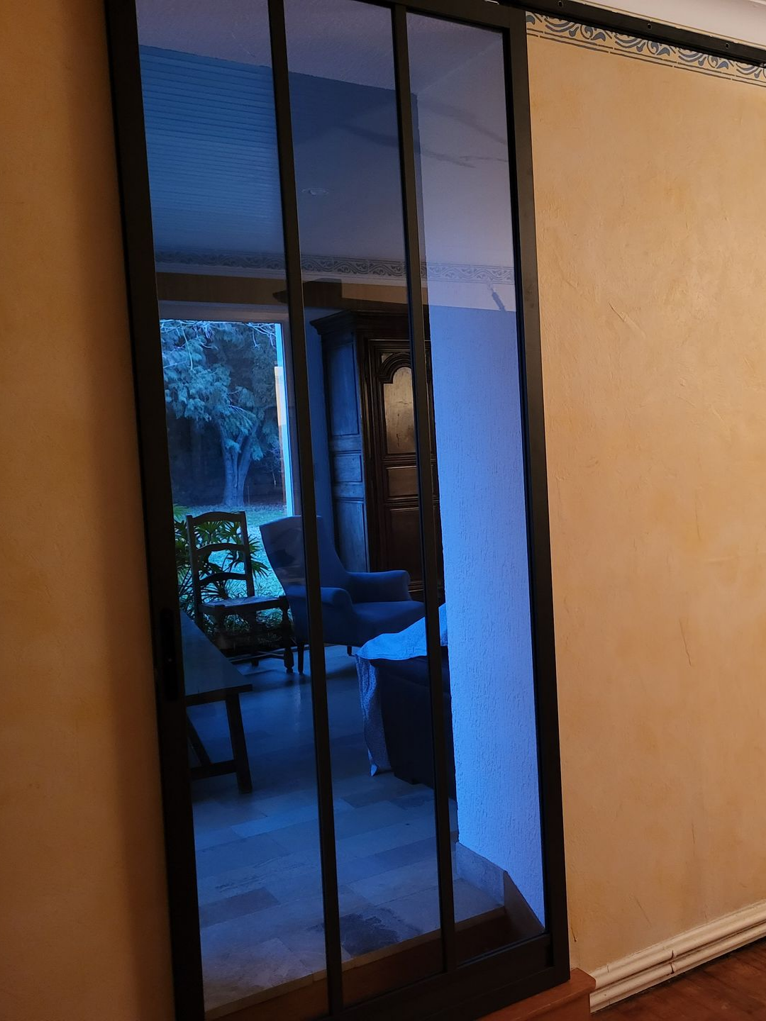 Porte coulissante en verre à cadre noir reflétant une scène extérieure aux reflets bleutés.