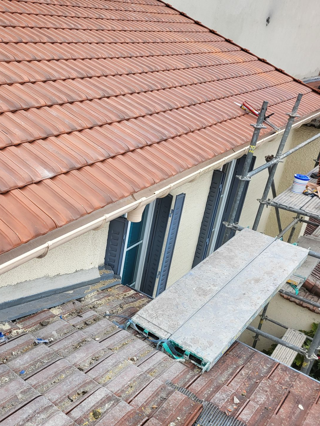 Travaux de réparation de toiture en cours : échafaudage, toiture en tuiles rouges, façade du bâtiment, planches.