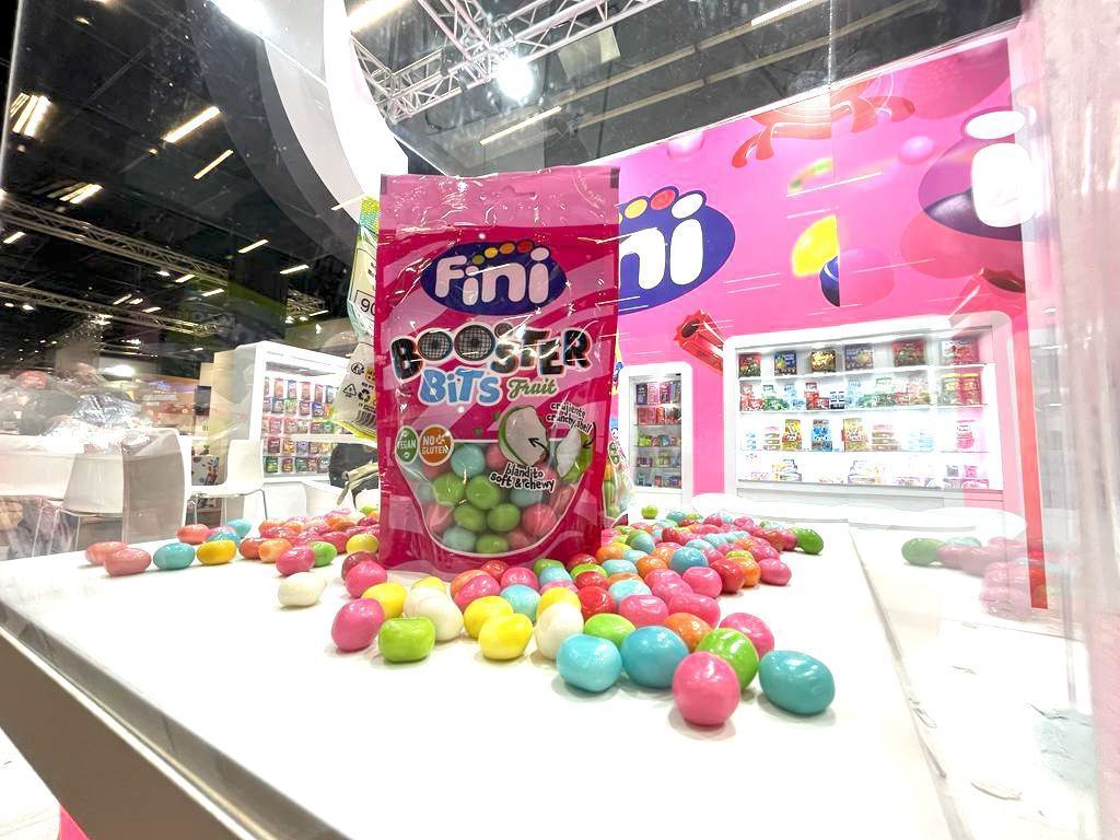 Caja de dulces Fini Croc'n Bits con dulces de colores dispersos sobre una superficie blanca, dentro de un expositor rosa.