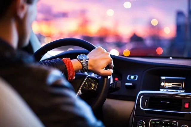 Un hombre conduce un coche por la noche y mira su reloj.