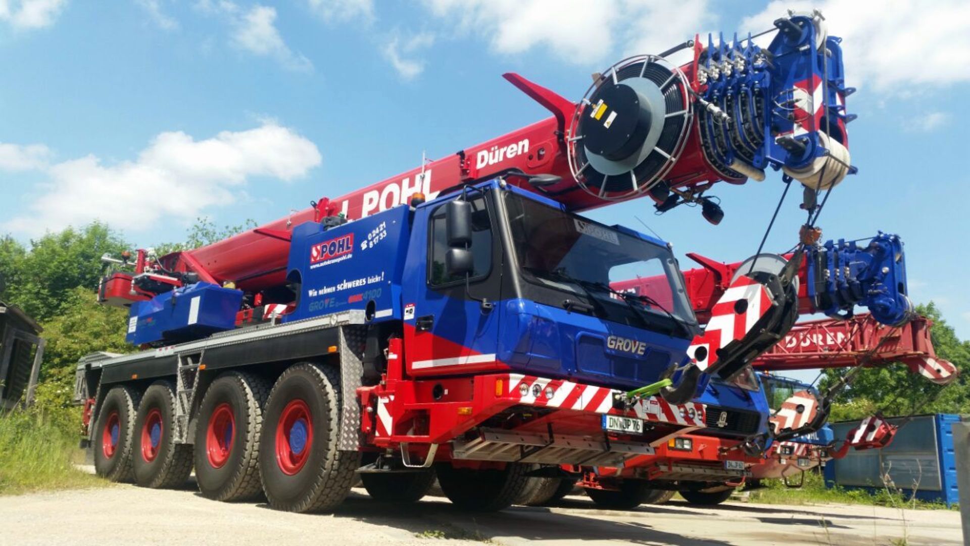 Ein rot-blauer Kranwagen steht neben einem anderen Kranwagen.