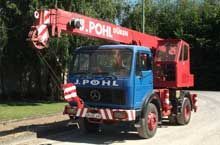 Ein rot-blauer Lastwagen mit einem Kran auf der Ladefläche steht am Straßenrand.