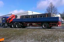 Ein blauer Lastwagen mit einem Kran auf der Ladefläche fährt eine Straße entlang.