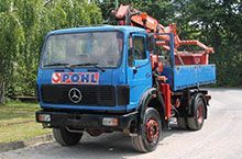 Ein blauer Lastwagen mit einem roten Kran auf der Ladefläche steht am Straßenrand.