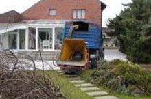 Ein blauer Lastwagen parkt vor einem Backsteinhaus.