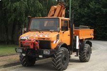 Ein orangefarbener Lastwagen mit einem Kran darauf steht am Straßenrand.