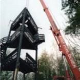 Ein roter Kran hebt im Wald einen Turm an.