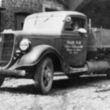 Ein Schwarzweißfoto eines alten Lastwagens, der vor einem Gebäude geparkt ist.