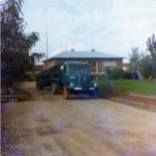 Ein blauer Lastwagen steht vor einem Haus an einer unbefestigten Straße.