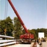 Ein großer roter Kran hebt einen Stapel Rohre an.