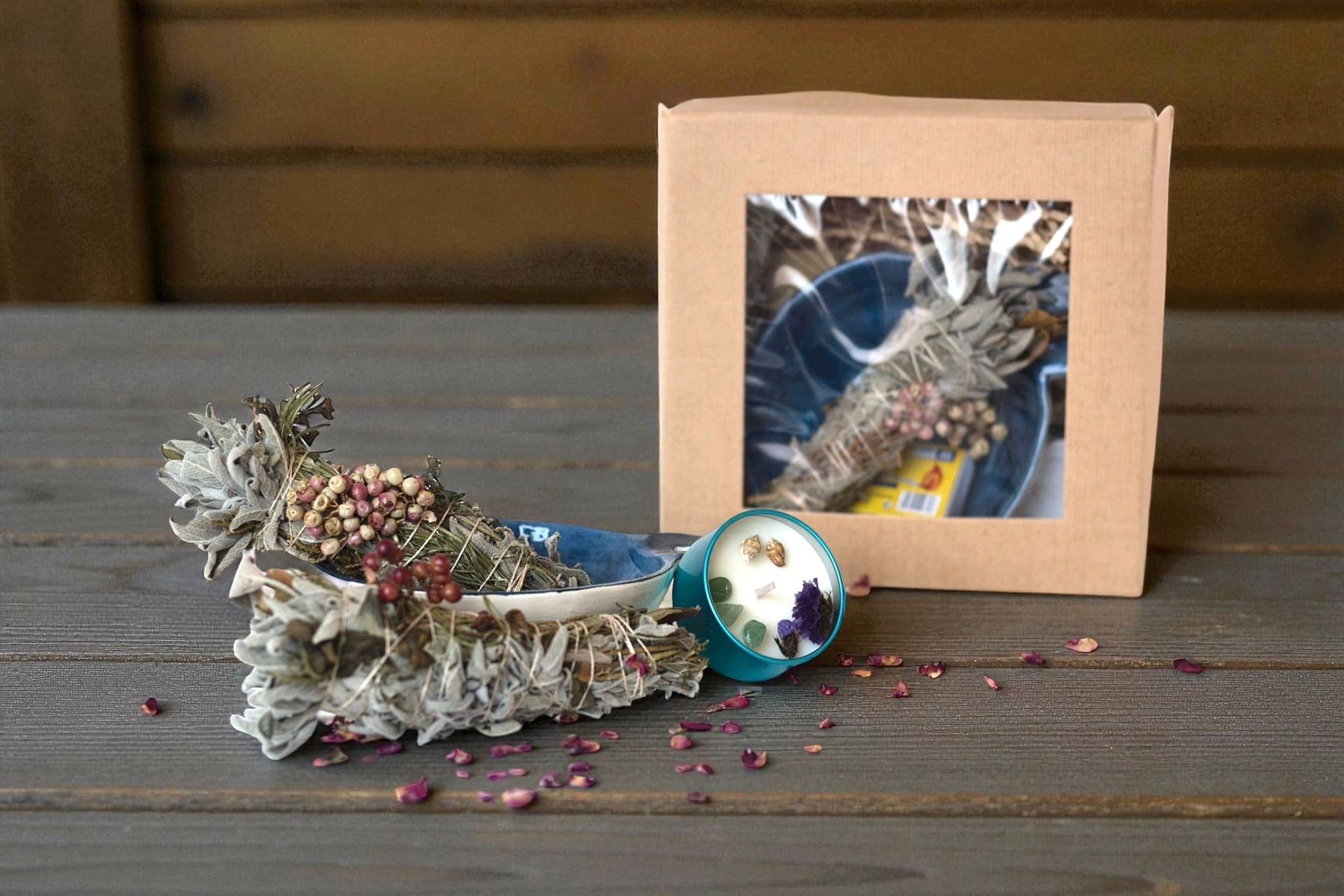 Un manojo de salvia con flores secas y una pequeña vela en una concha turquesa junto a una caja.