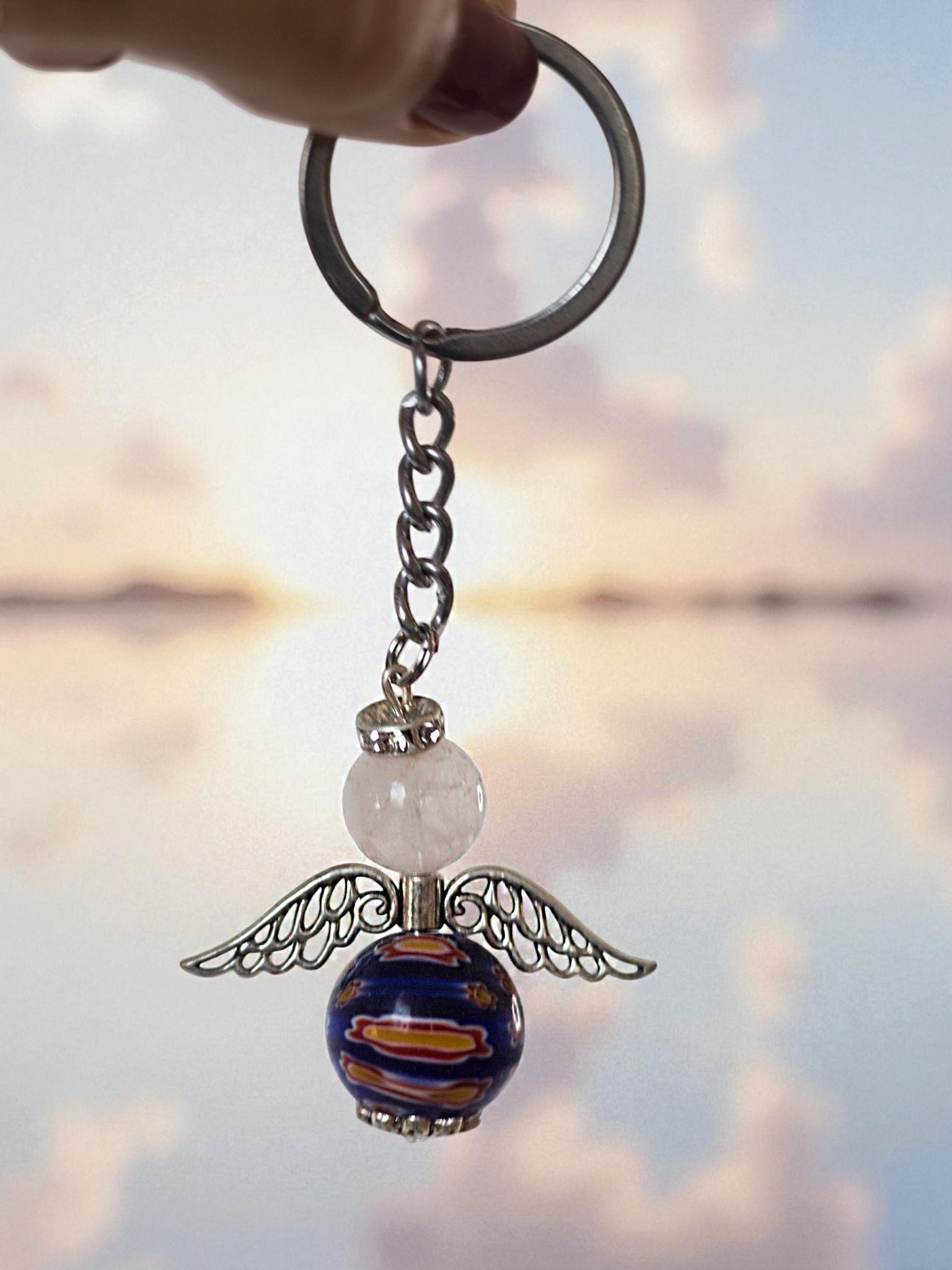 Llavero con dije de ángel, sostenido contra un fondo de puesta de sol borrosa.