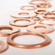 Arandelas de cobre dispuestas sobre una superficie blanca, de varios tamaños visibles.