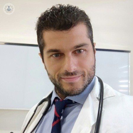 Un hombre vestido con una bata blanca y corbata con un estetoscopio alrededor del cuello.