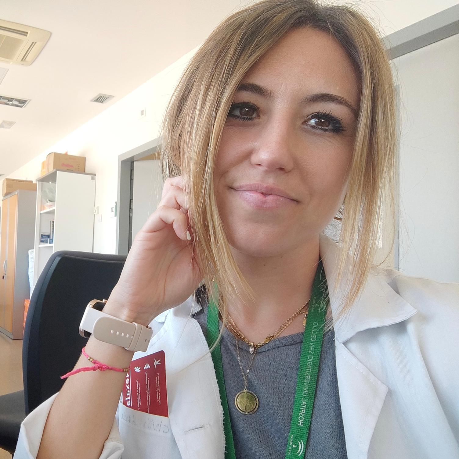 Una mujer que lleva una bata de laboratorio blanca y un cordón verde está sonriendo.