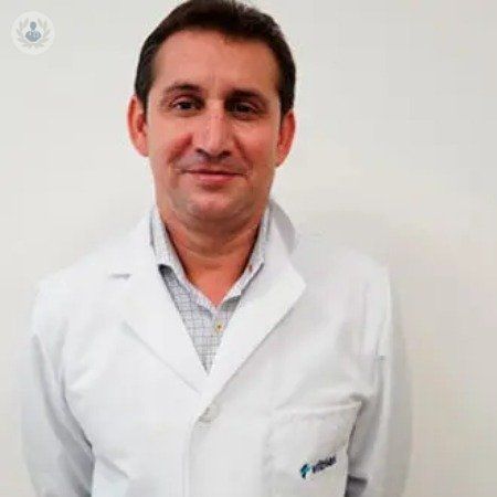 Un hombre con una bata blanca está parado frente a una pared blanca.