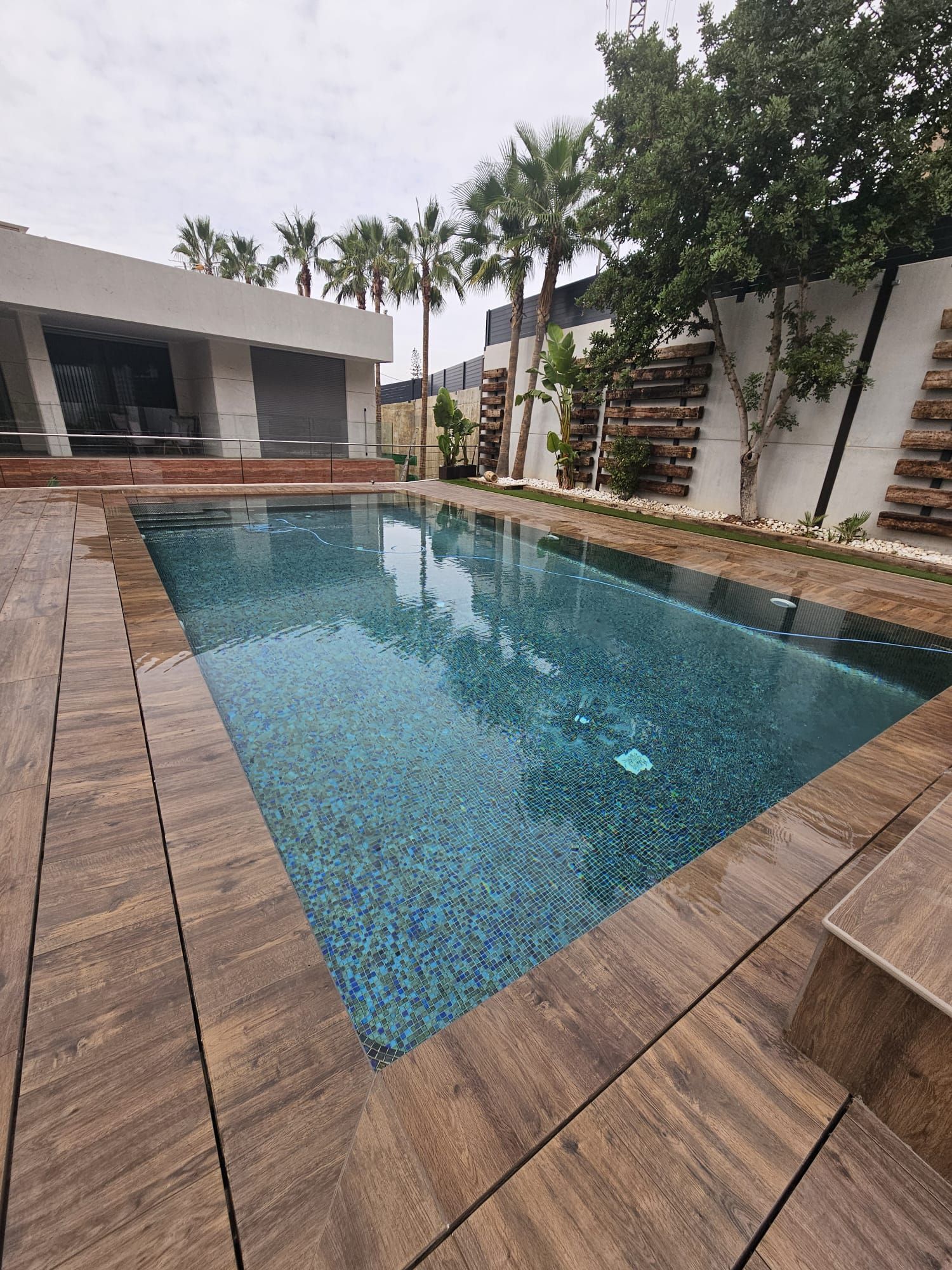 Una gran piscina rodeada de palmeras y un deck de madera.