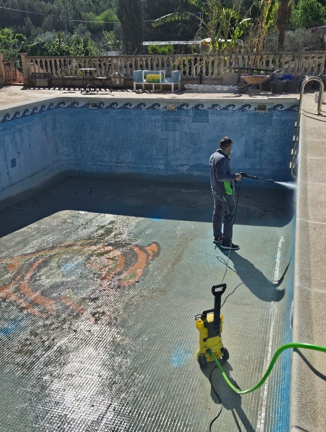 Un hombre está limpiando una piscina con una hidrolavadora.