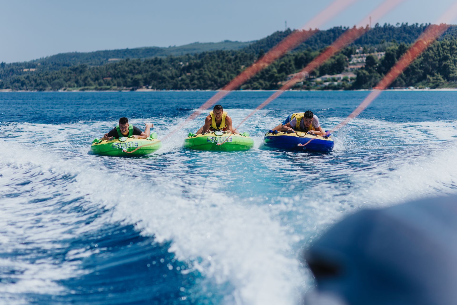 Trois personnes sur des bouées tractées par un bateau en mer.