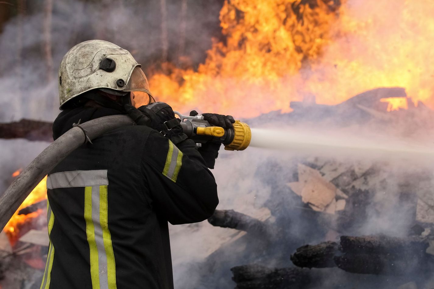 Un pompier arrose une structure en feu, les flammes étant visibles en arrière-plan.
