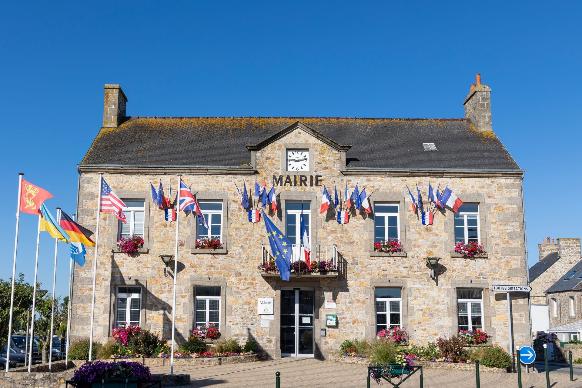 Bâtiment en pierre avec le panneau Mairie, drapeaux flottants.