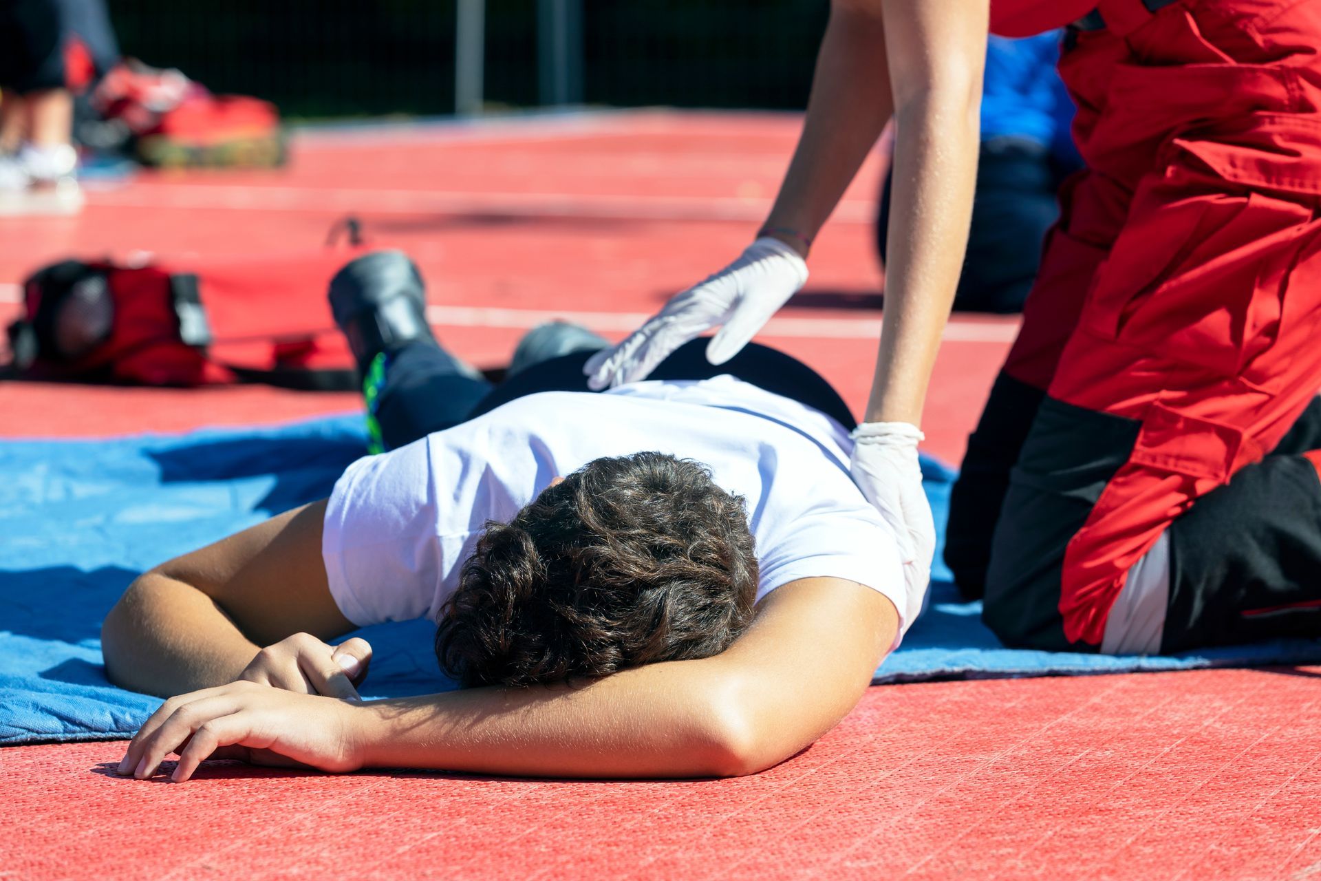Une personne allongée sur un terrain d'athlétisme est secourue par une personne en tenue médicale.