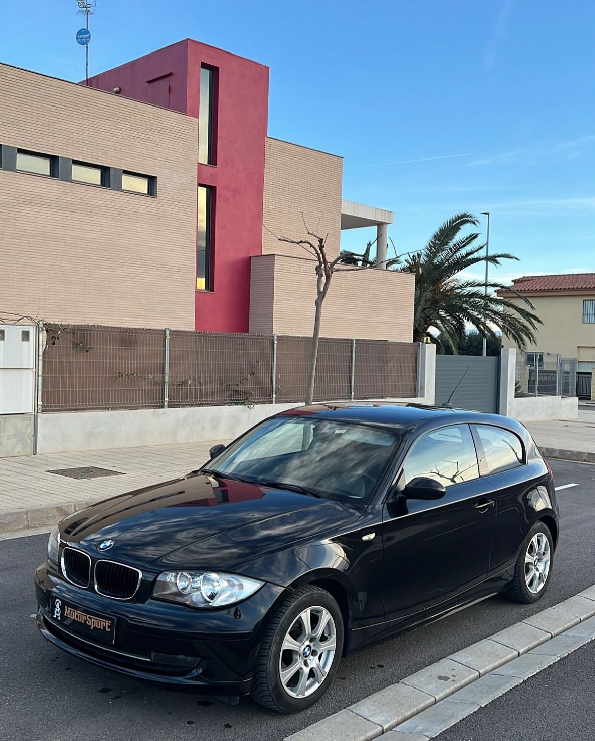 Un automóvil BMW Serie 1 de color negro estacionado en una calle frente a una casa moderna.