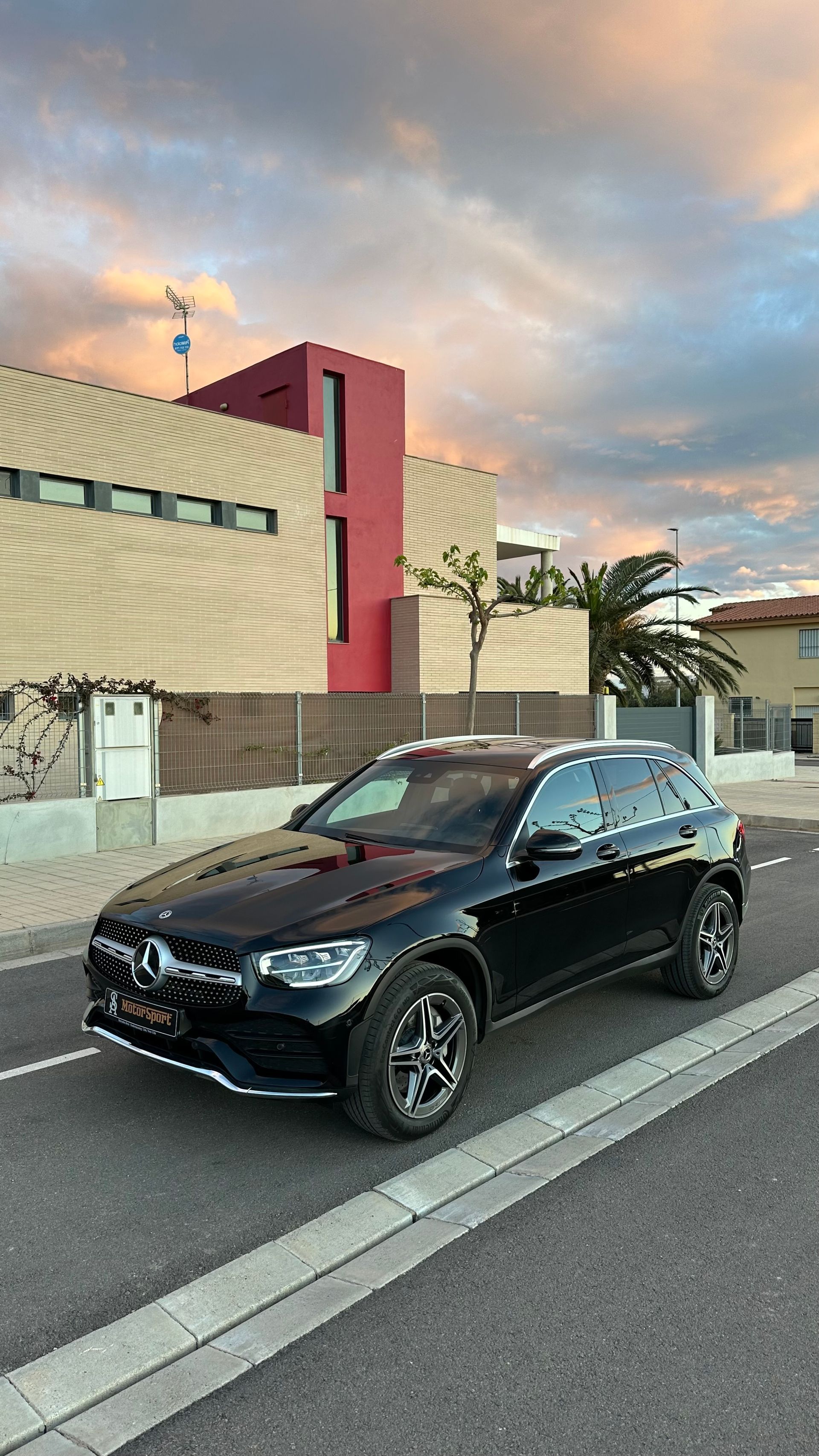 SUV Mercedes negro estacionado en una calle frente a una casa moderna al atardecer.