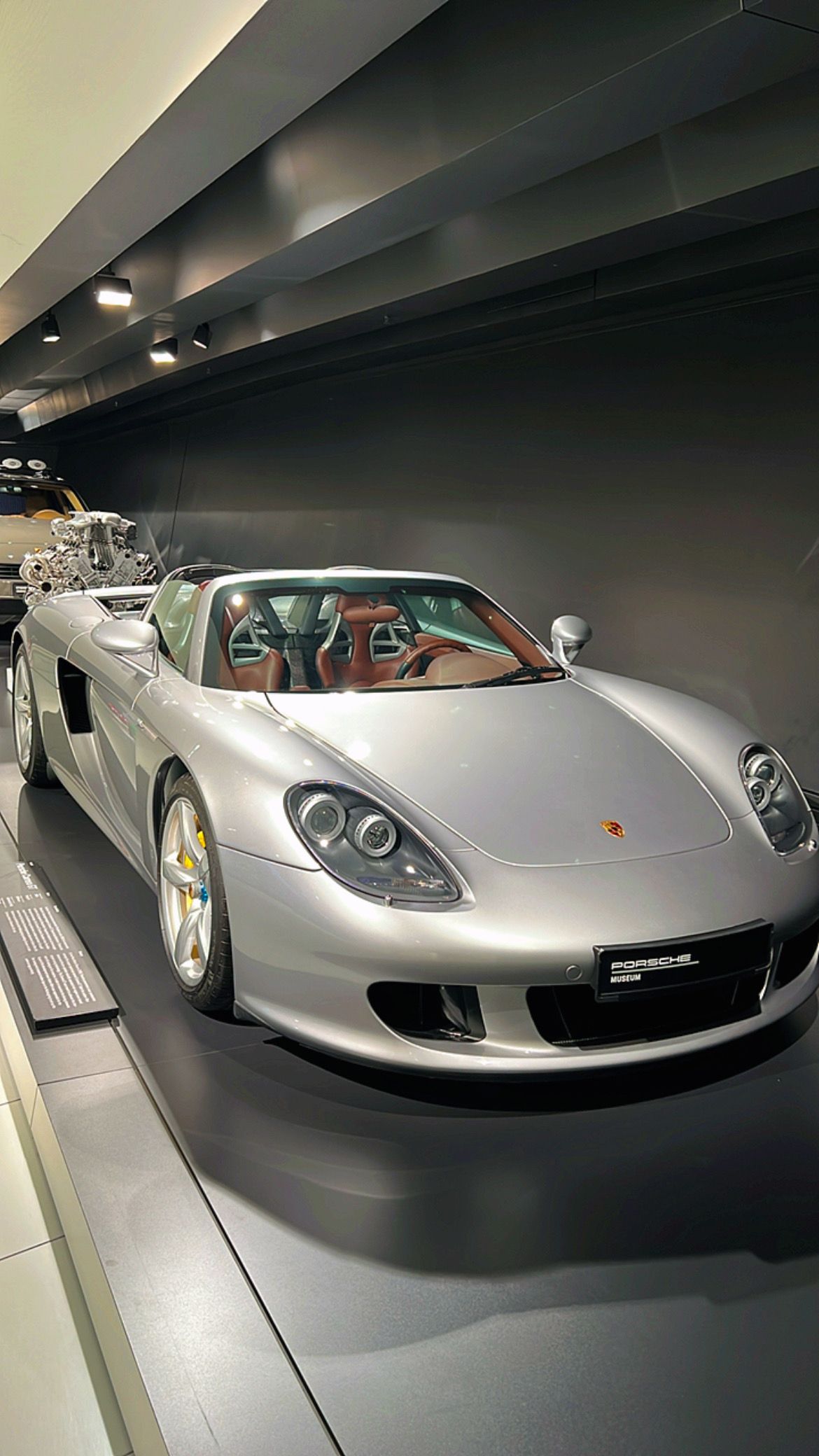 Porsche Carrera GT convertible plateado expuesto en un museo.