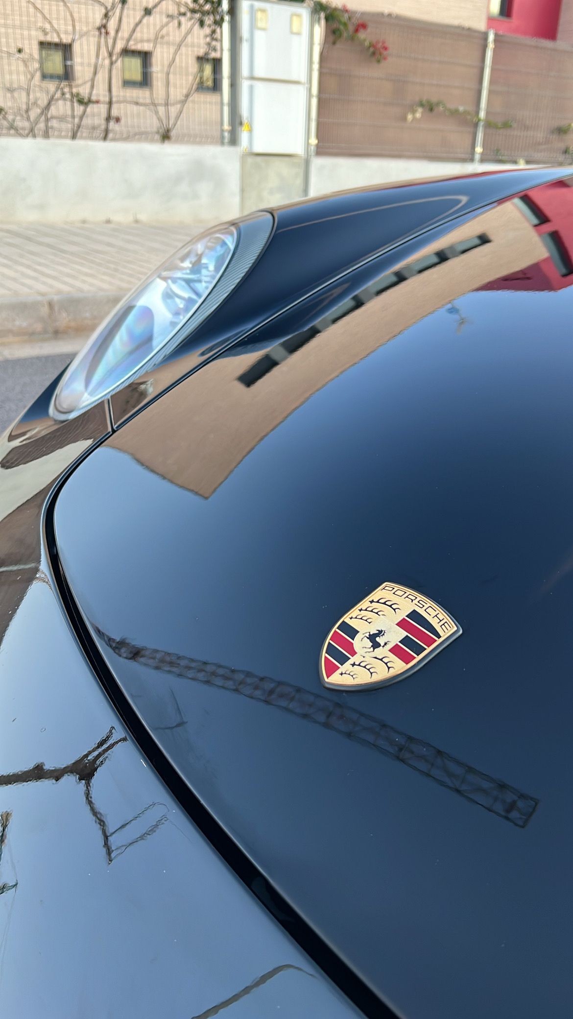 Capó de coche Porsche de color negro con emblema que refleja el entorno.