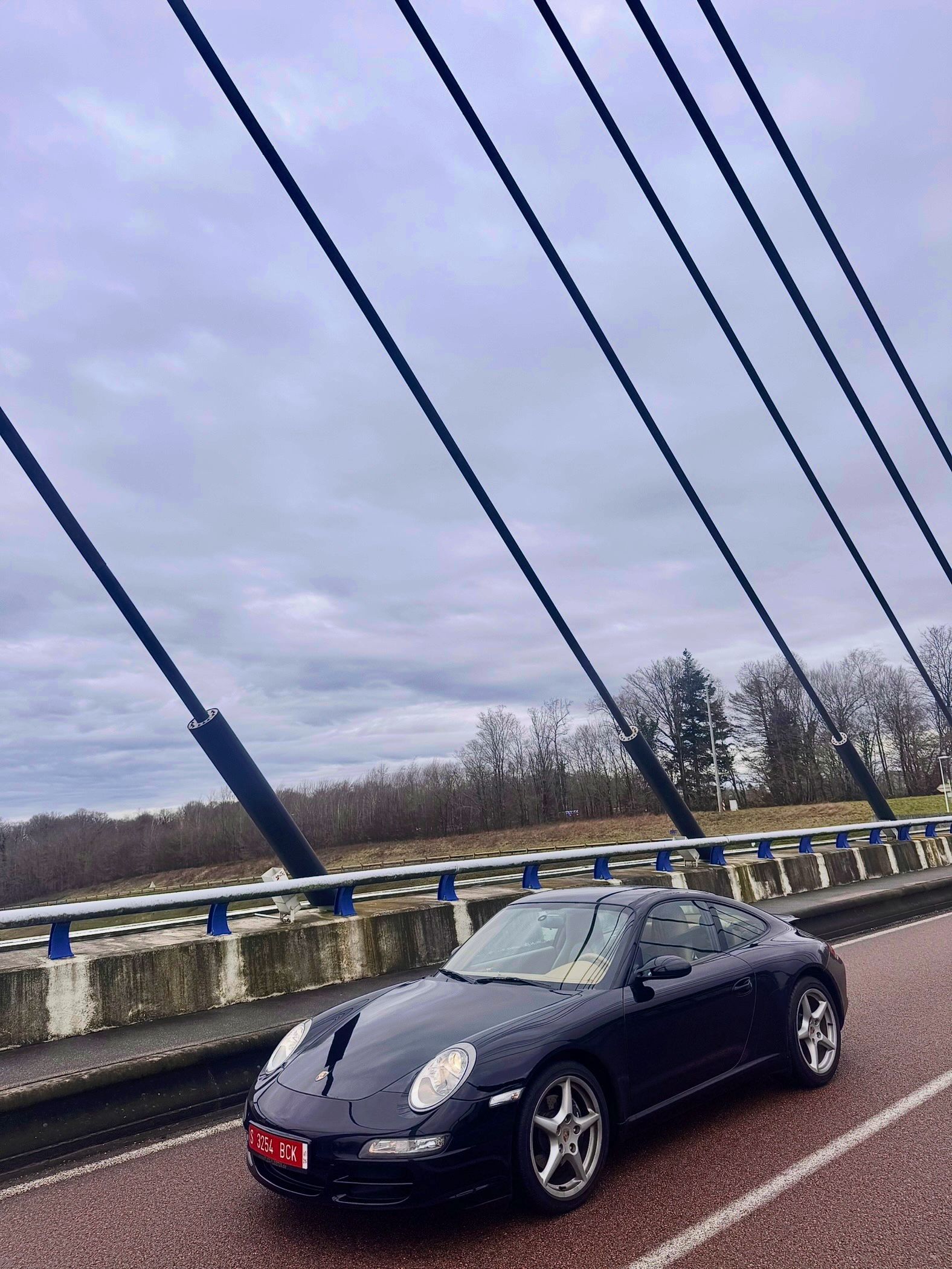 Coche deportivo Porsche negro en un puente, bajo un cielo nublado.