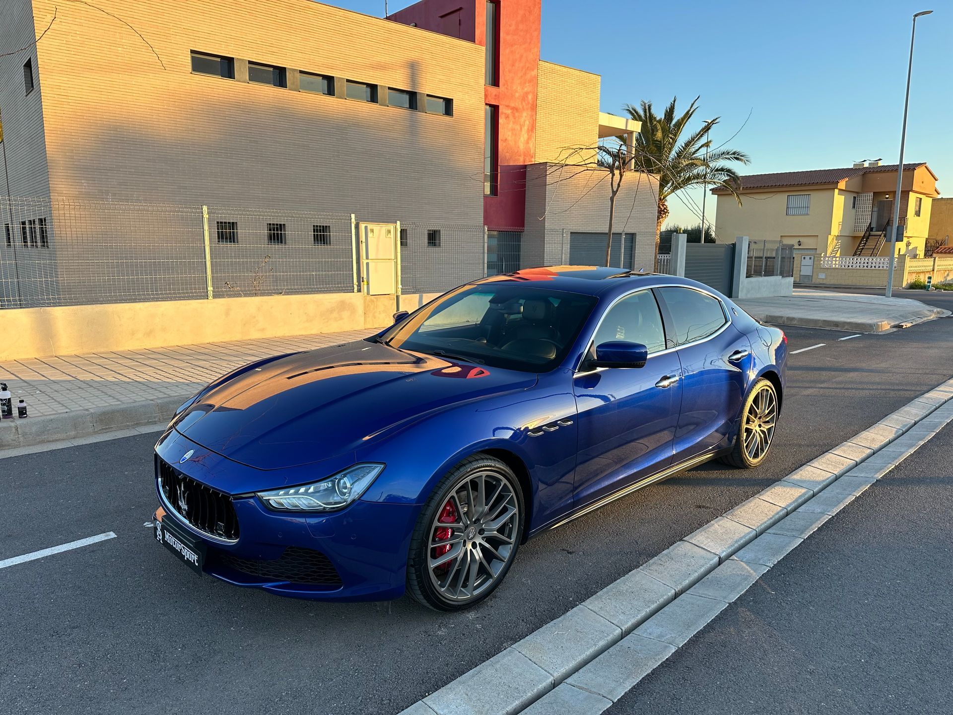 Maserati Ghibli azul estacionado en una calle frente a un edificio con iluminación cálida.