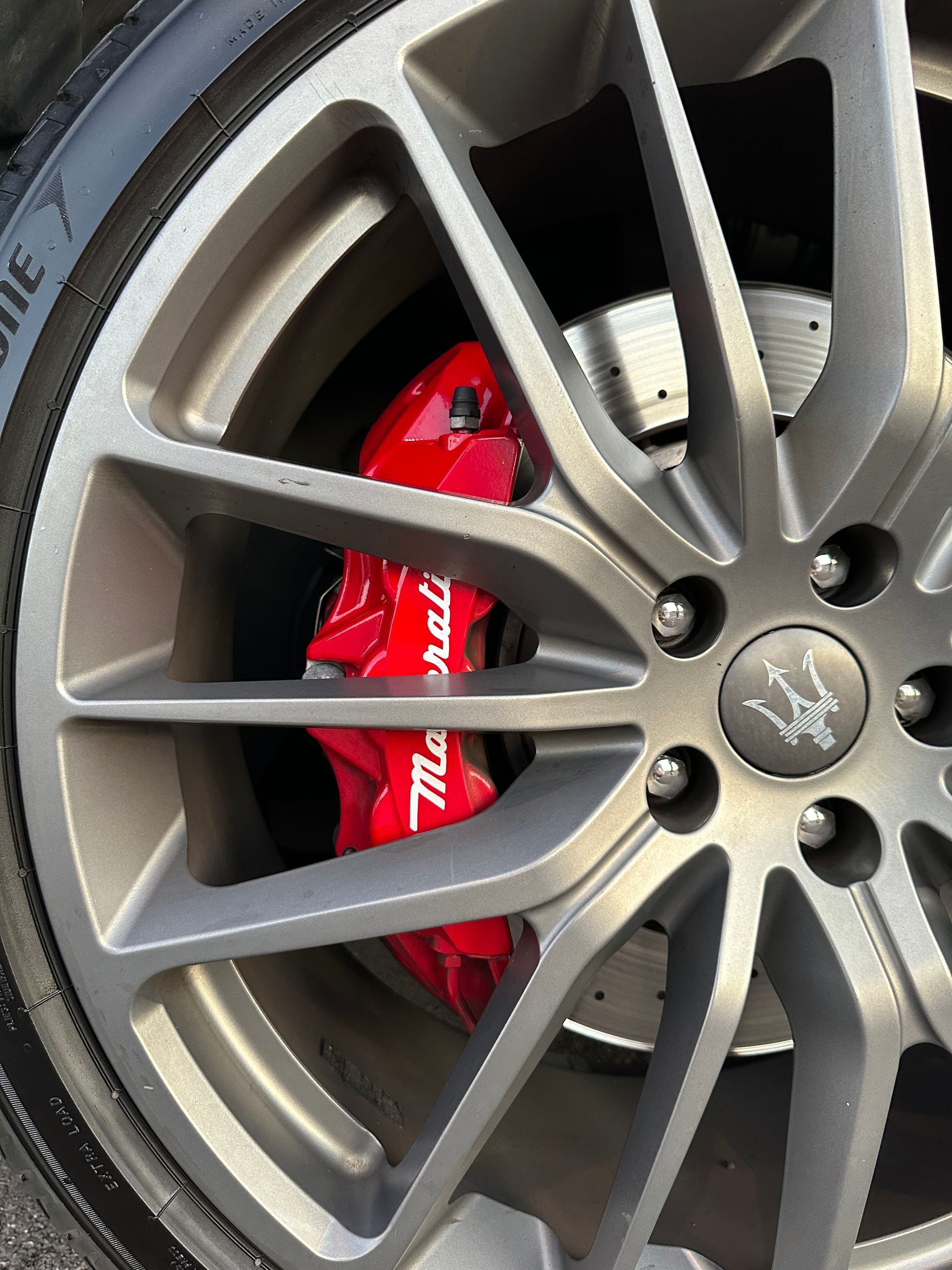 Primer plano de una rueda de coche plateada con una pinza de freno Maserati de color rojo.