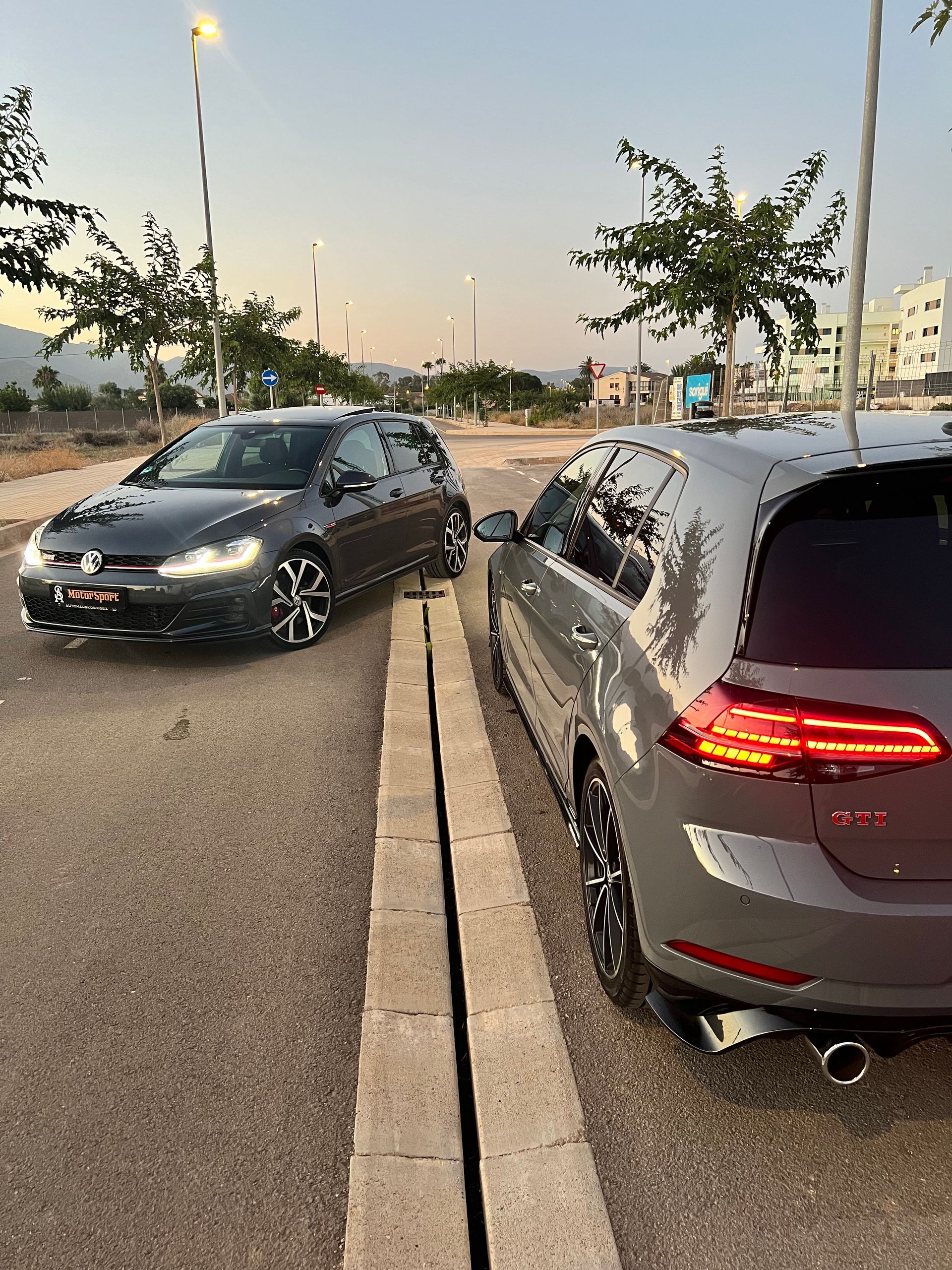 Dos Volkswagen Golf grises estacionados uno al lado del otro en una carretera junto a un canal de drenaje de hormigón.