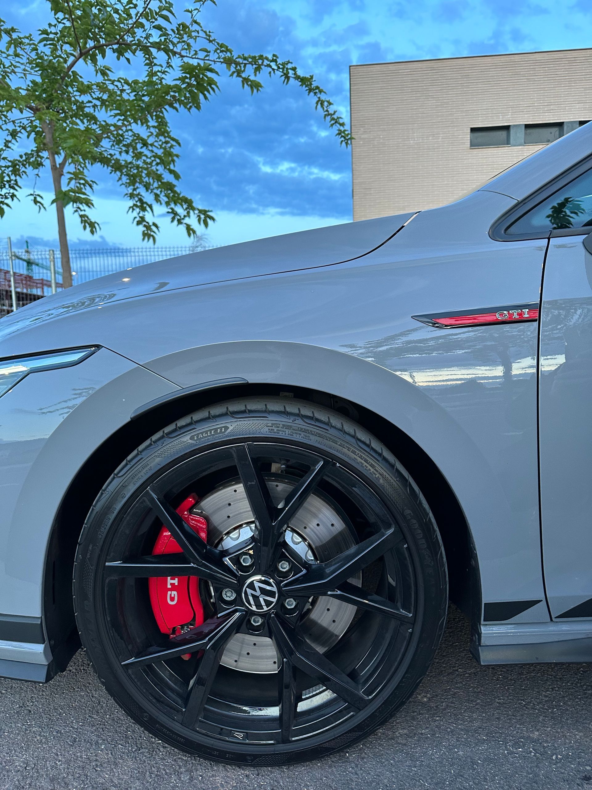 VW Golf GTI gris, llantas negras, pinzas de freno rojas, estacionado en el exterior.