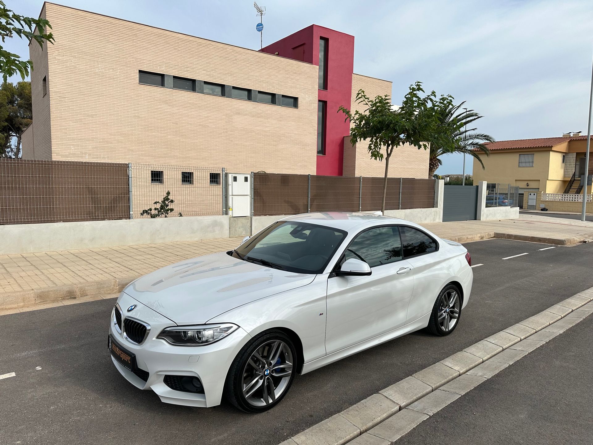 Un BMW cupé blanco estacionado en una calle frente a una casa moderna.