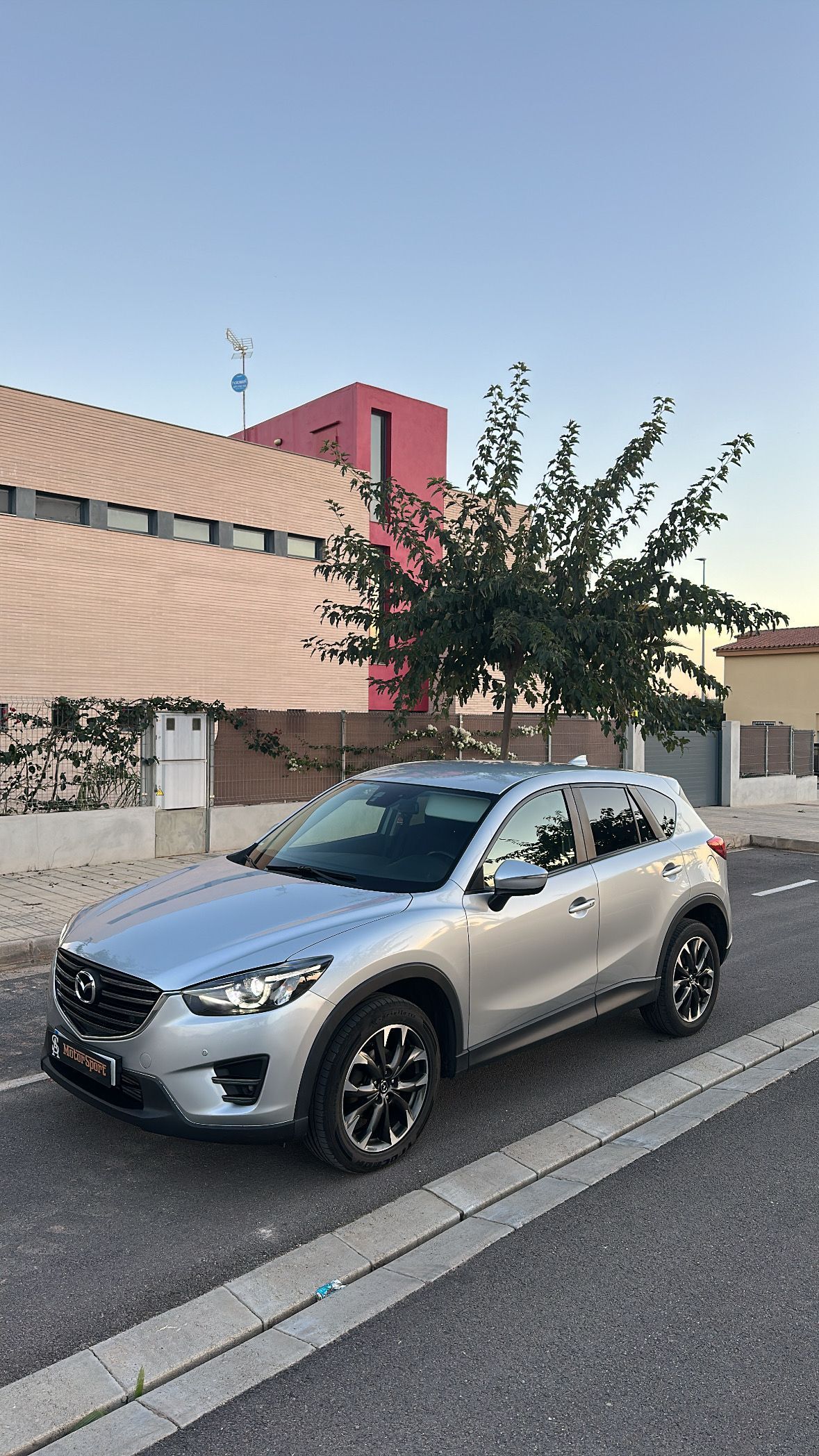 SUV Mazda CX-5 color plata estacionada en una calle pavimentada frente a una casa.