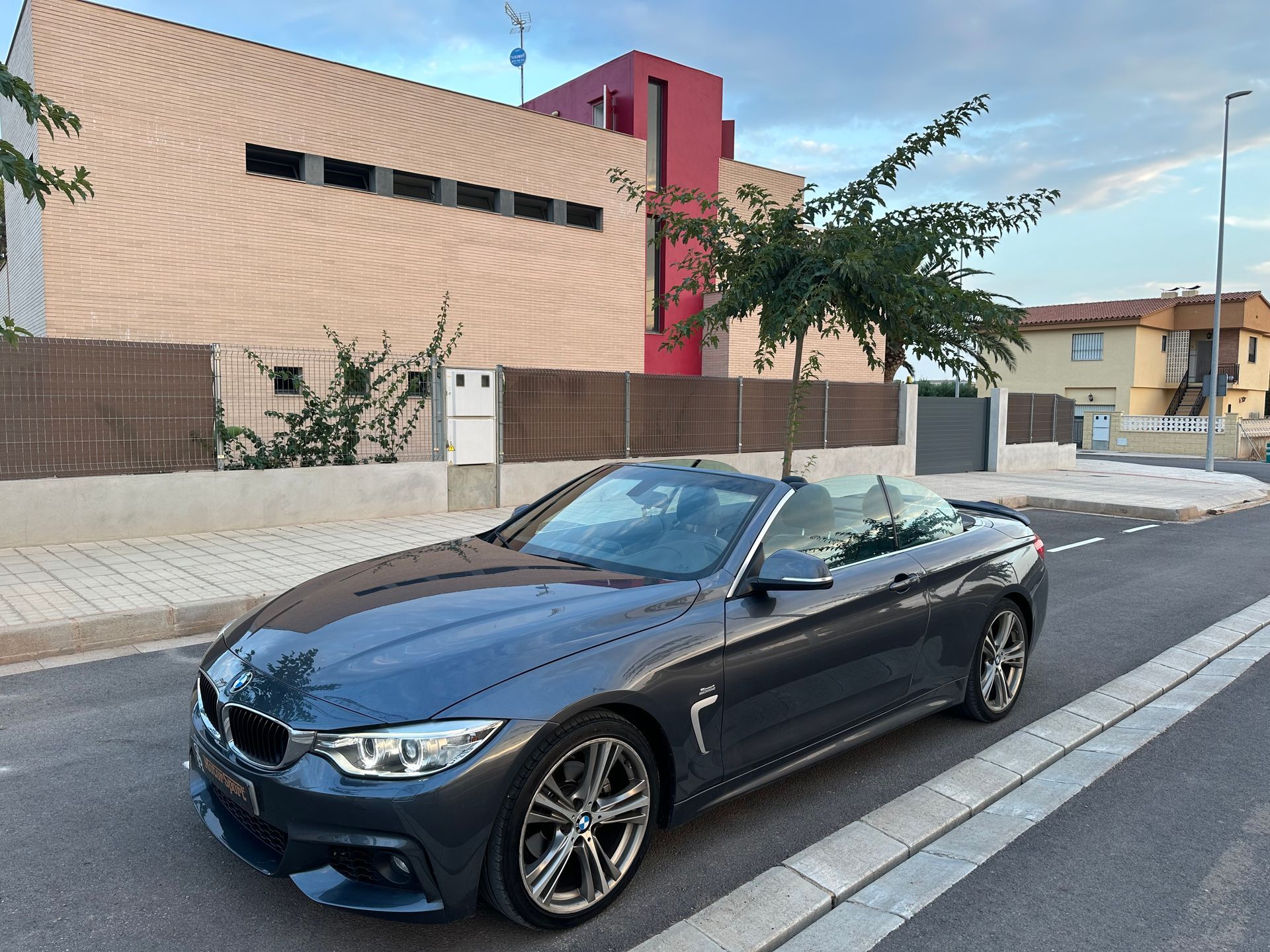 BMW convertible gris estacionado en una calle frente a una casa moderna.