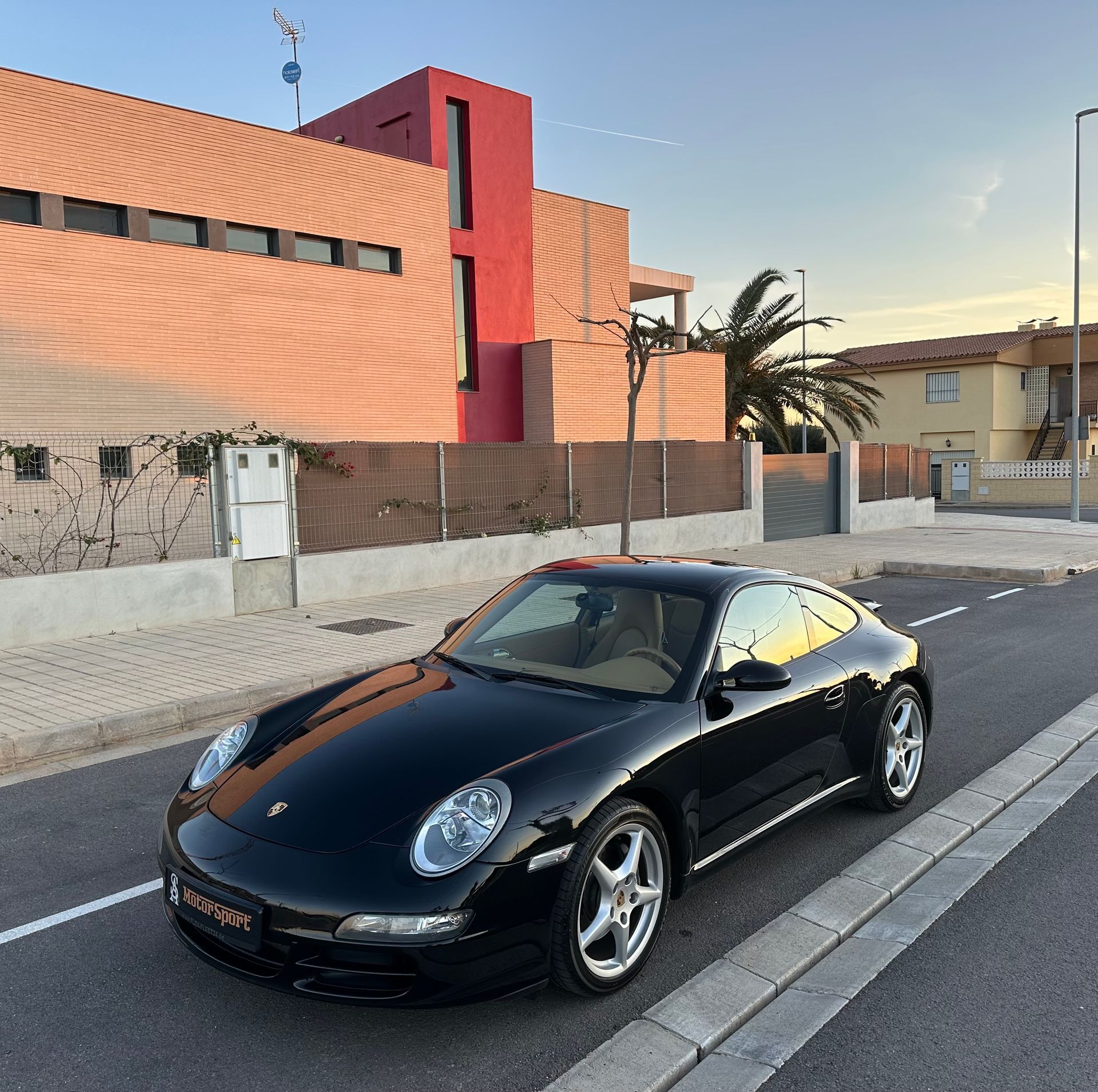 Coche deportivo Porsche negro aparcado en una calle frente a un edificio moderno.