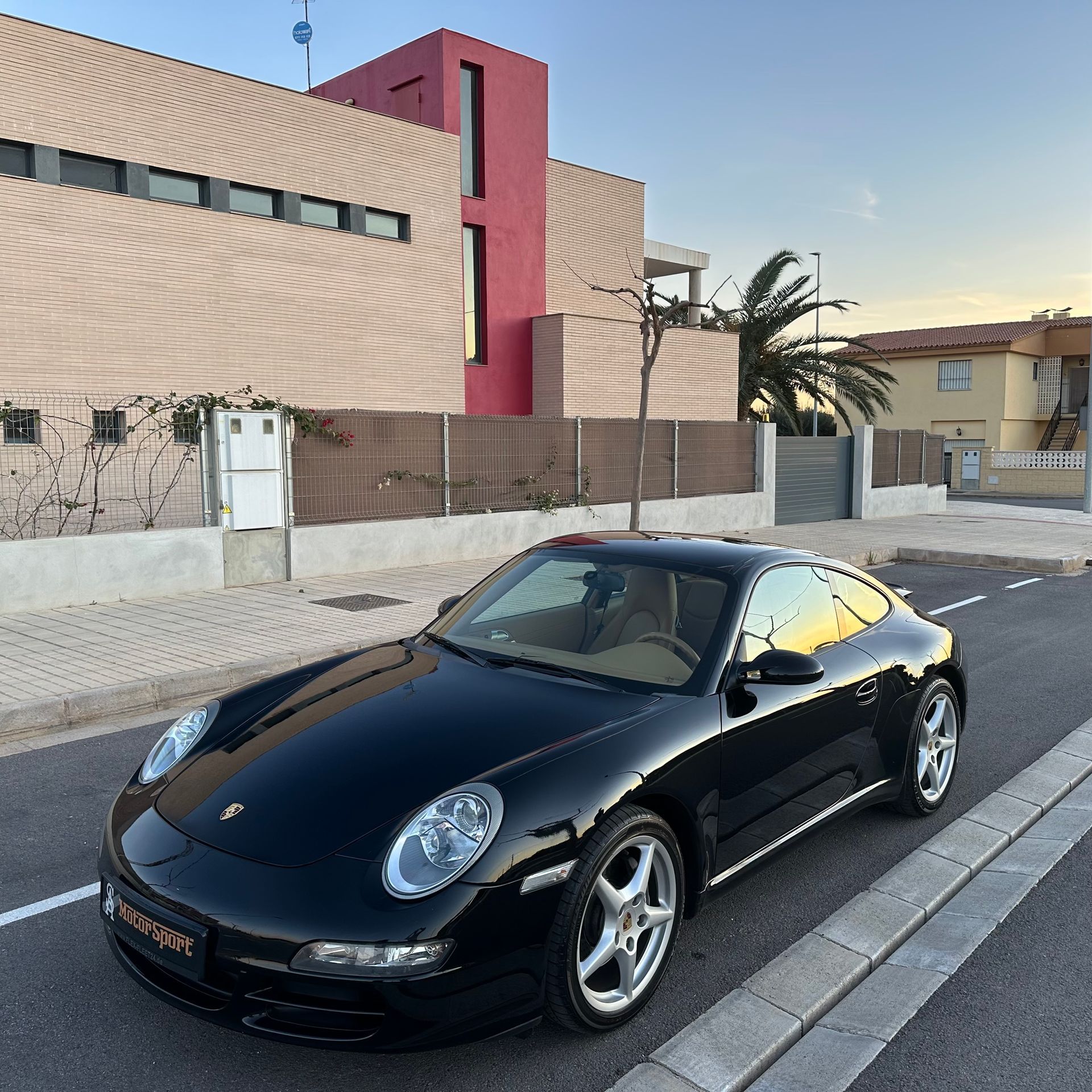 Porsche 911 negro estacionado en una calle frente a una casa moderna.