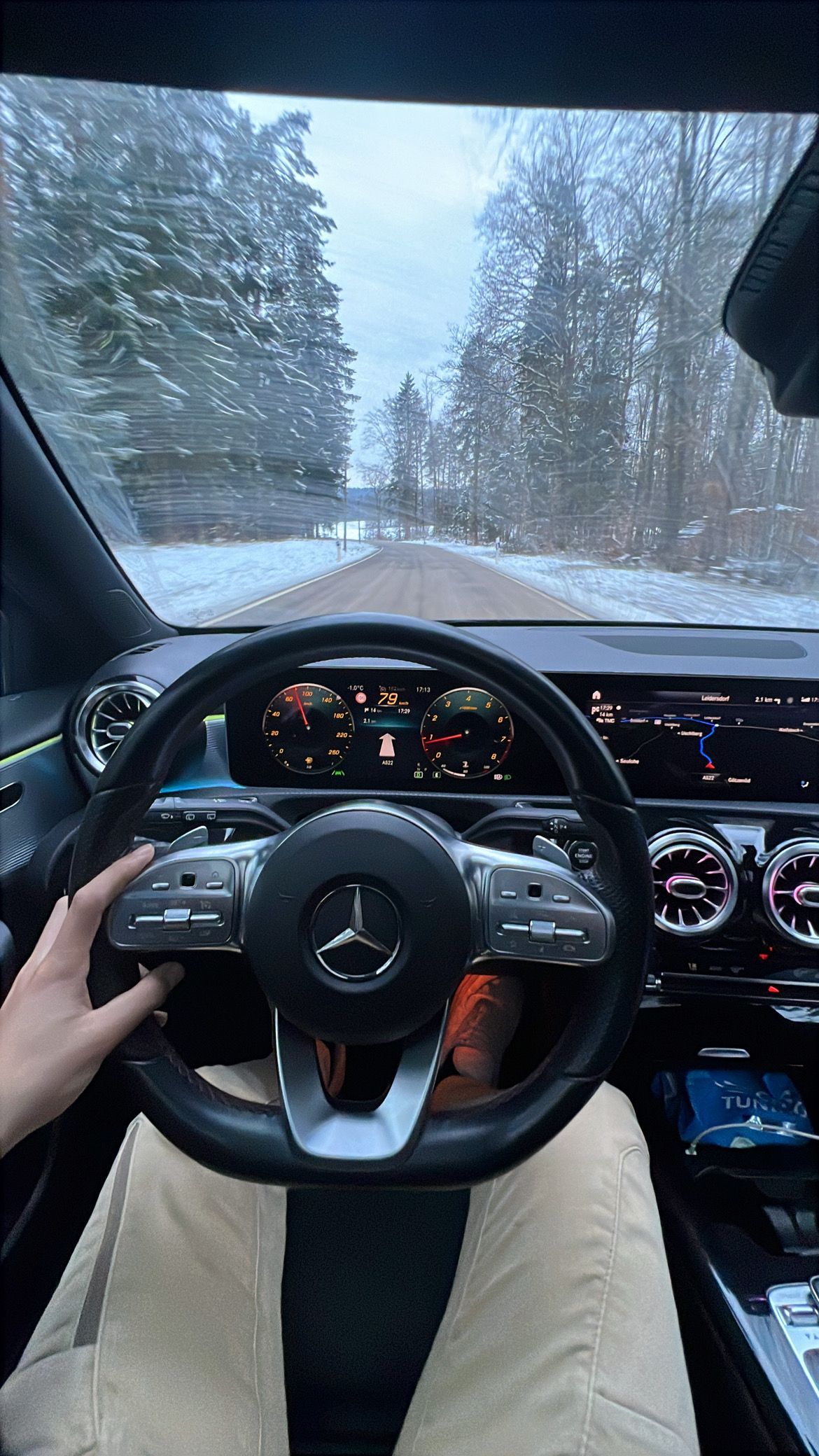 Perspectiva del conductor dentro de un Mercedes-Benz, conduciendo por una carretera nevada a través de un bosque.
