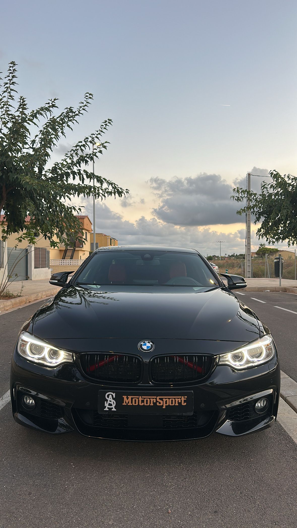 Coche BMW negro estacionado en una carretera, vista frontal, bajo un cielo nublado.