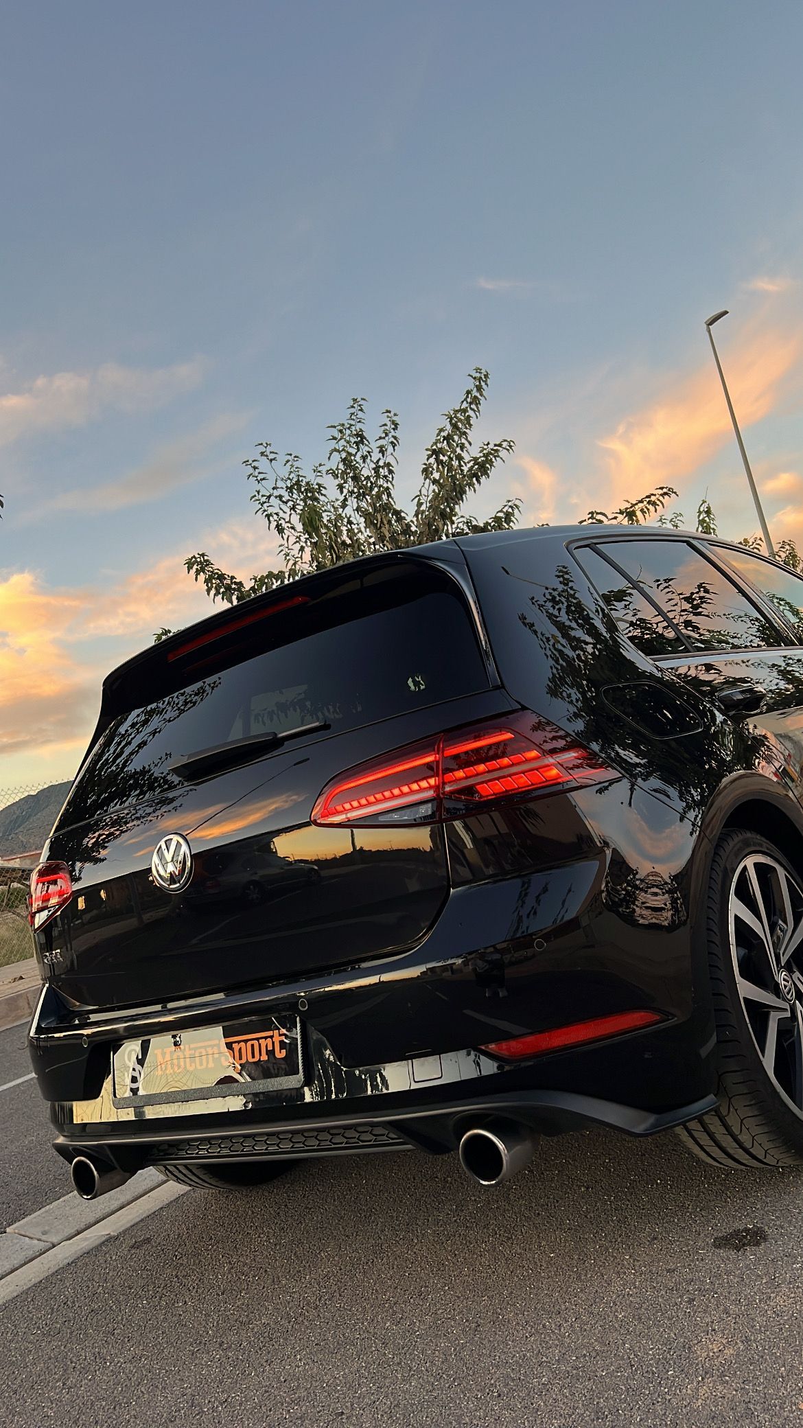 Volkswagen Golf R negro estacionado al costado de una carretera al anochecer; luces traseras encendidas.