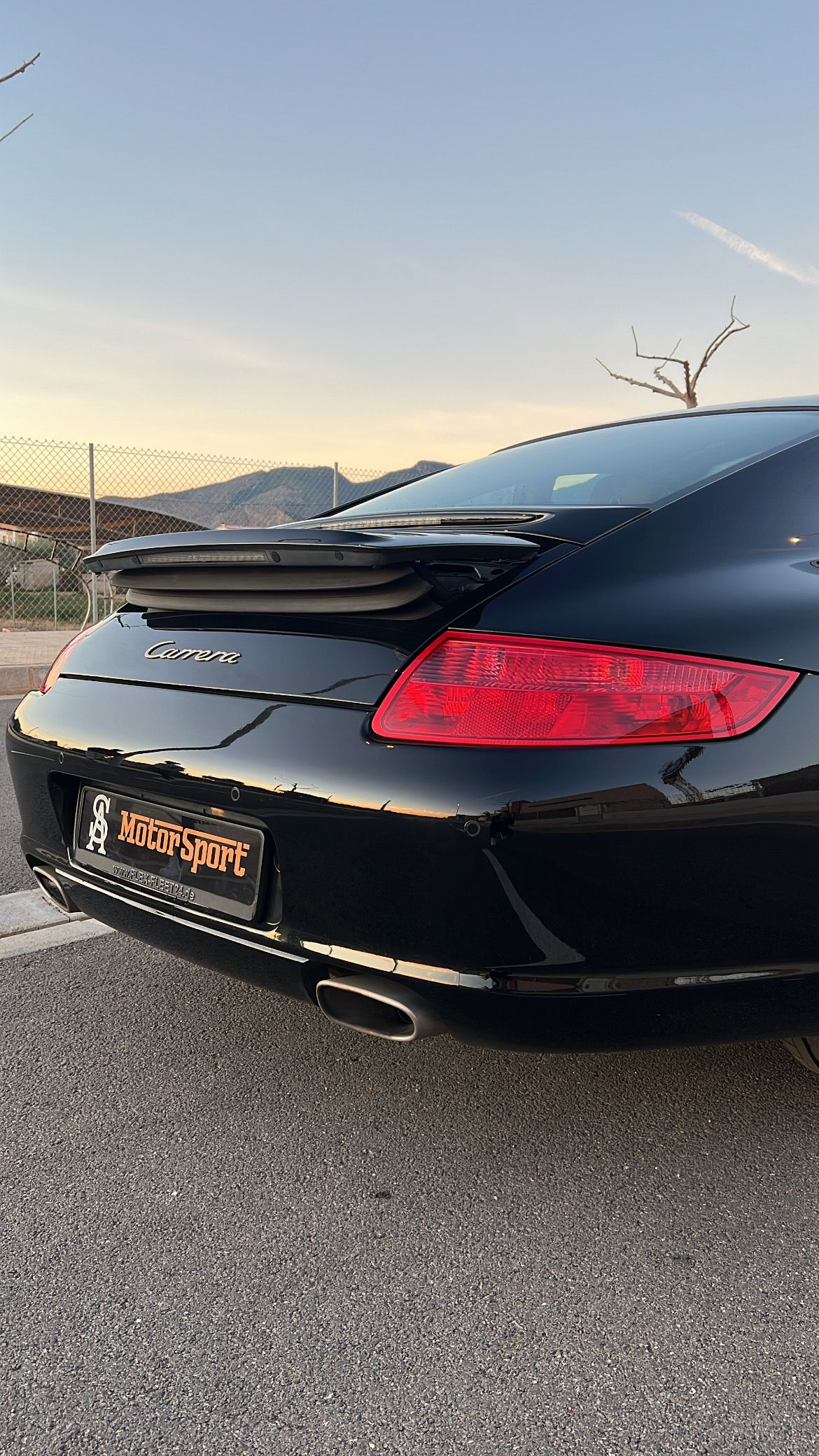 Deportivo negro, vista trasera, en un estacionamiento. Se ven la luz trasera roja, el alerón y la matrícula.