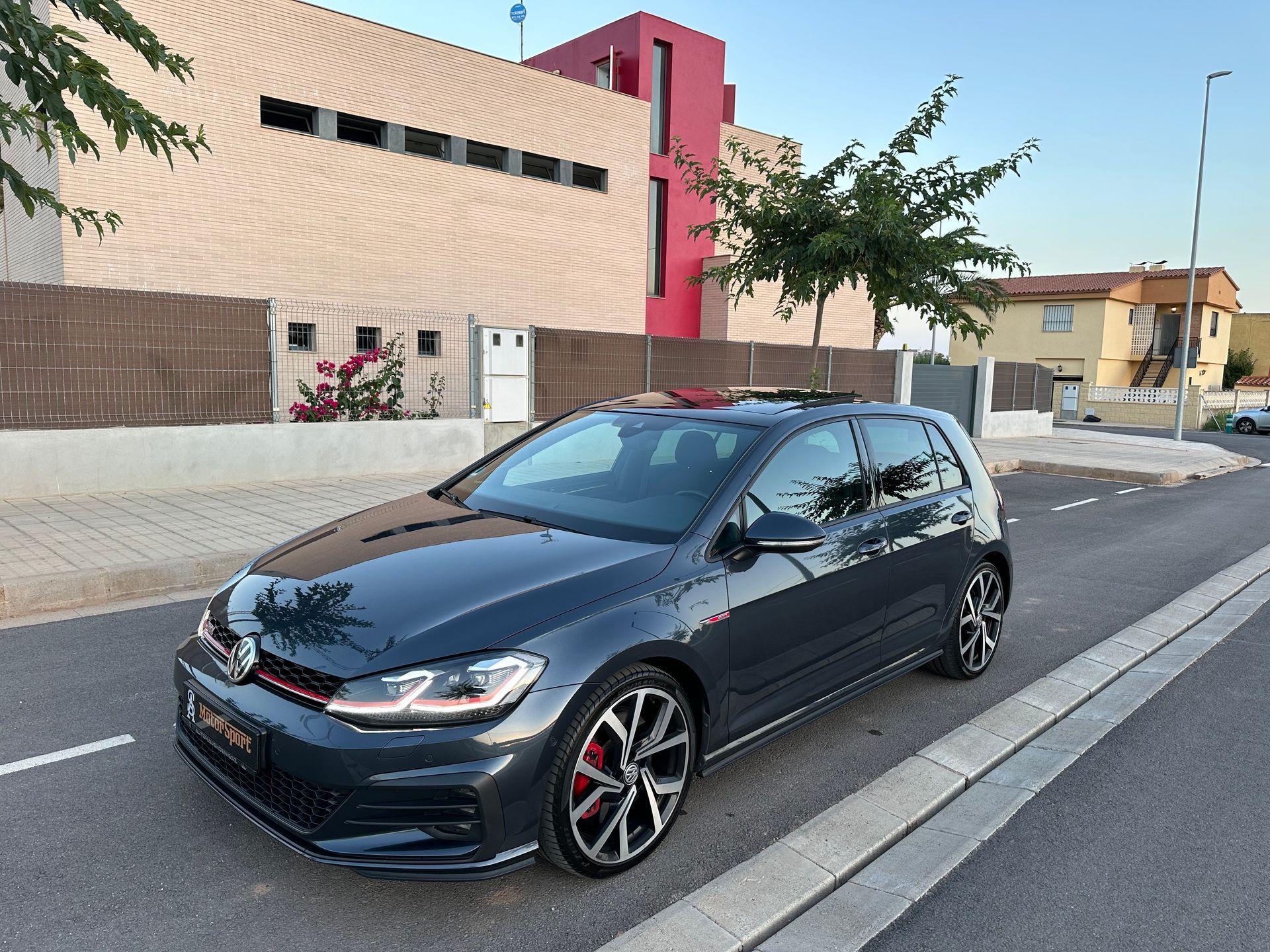 Volkswagen Golf GTI gris oscuro estacionado al costado de una carretera, frente a una casa moderna.