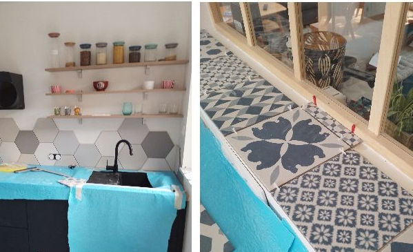 Cuisine avec crédence hexagonale, étagères avec bocaux et bols, évier noir. Carrelage bleu et à motifs près de la fenêtre.