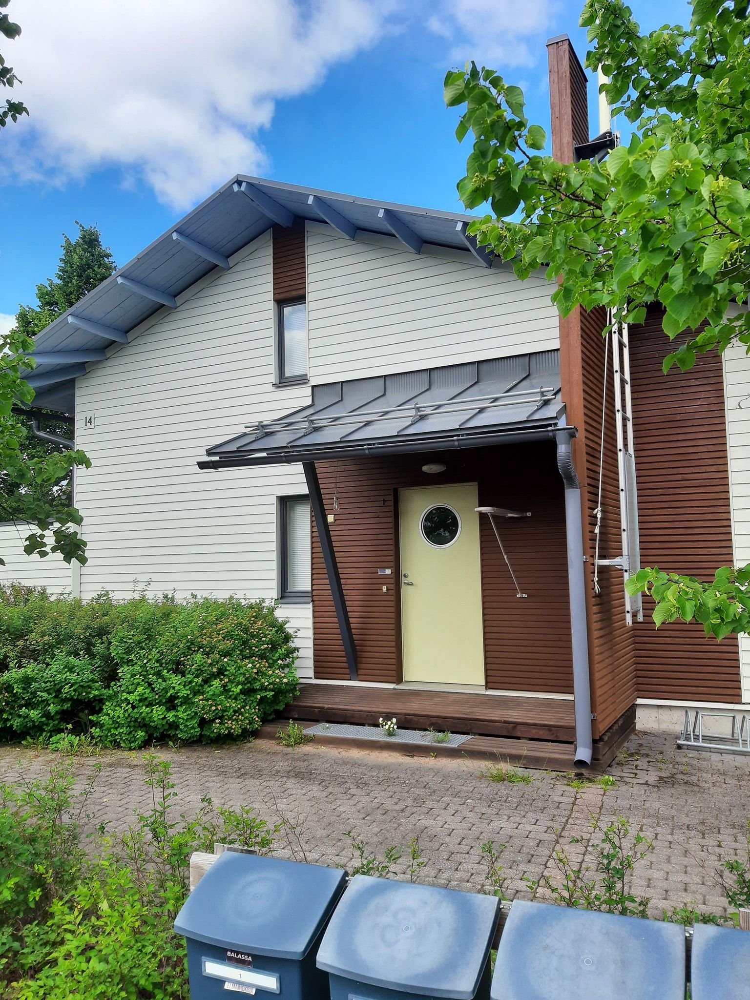 Kaksikerroksinen talo, jossa on aurinkopaneelit katolla, vaaleanvihreä ovi, ruskea ulkoverhous