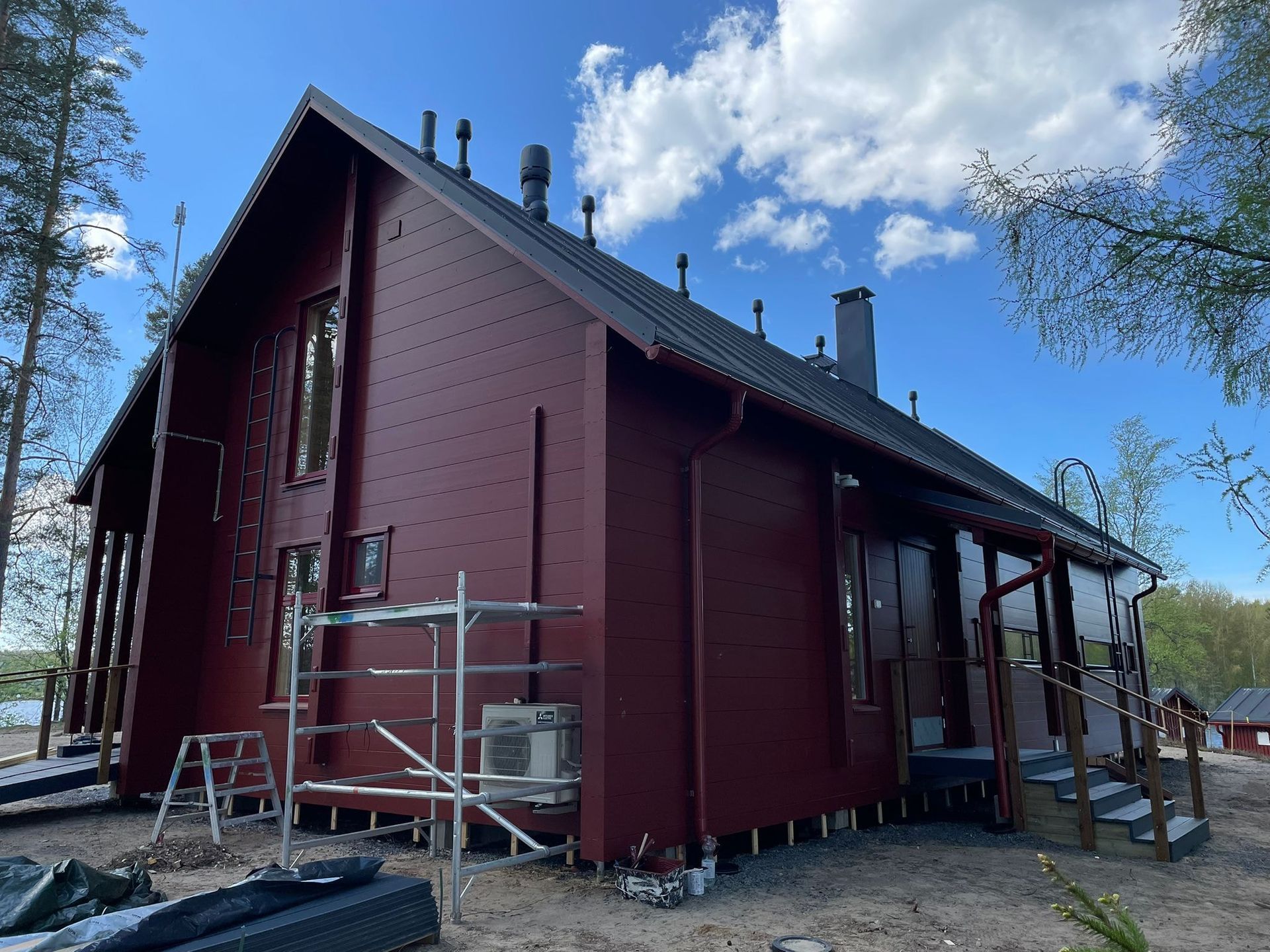 Punainen puinen talo rakenteilla, jossa on rakennustelineet ja portaat.