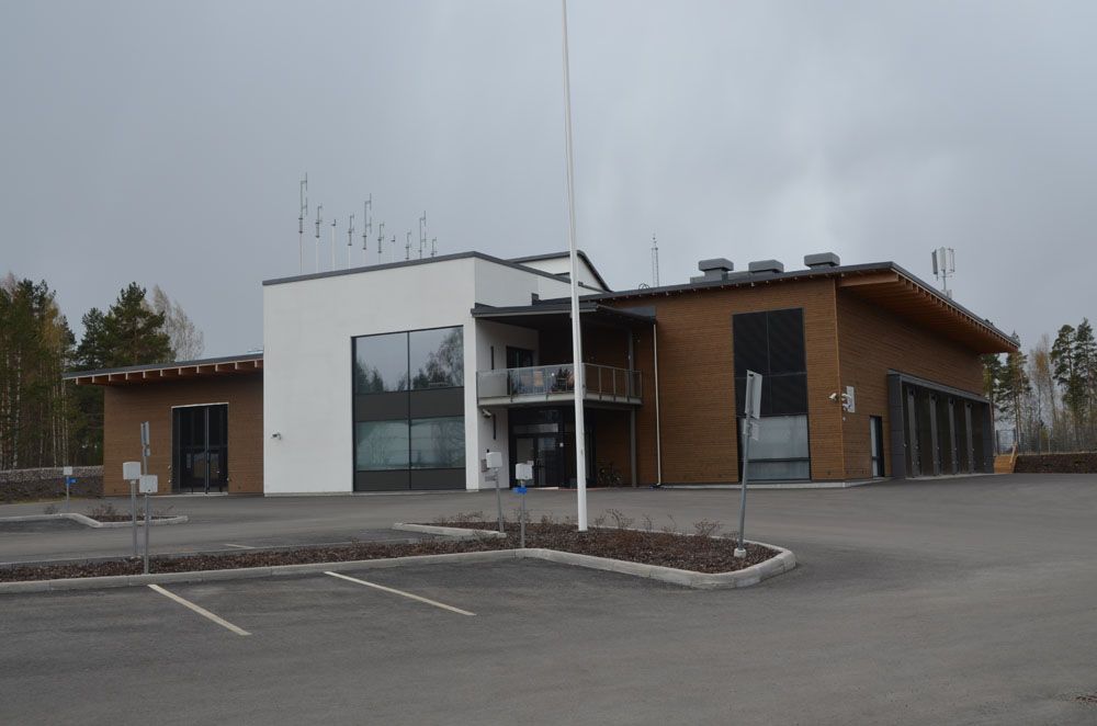 Moderni rakennus, jossa on valkoinen ja ruskea ulkopinta, pysäköintialue ja pilvinen taivas.